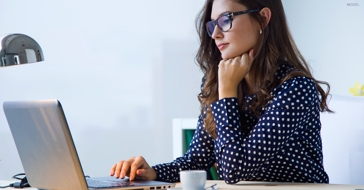 Brunette woman looking at computer researching breast augmentation.