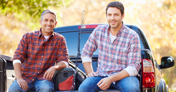 Two men sitting on the bed of a truck.