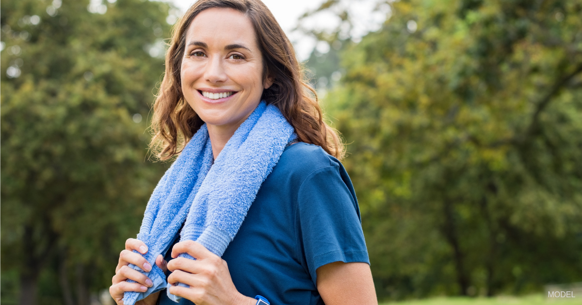 A woman considering body contouring after weight loss holds a towel around her neck following an intense exercise workout